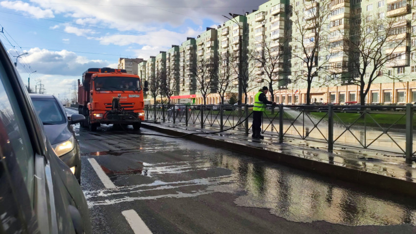 Рабочий моет дорожное ограждение рядом с коммунальной спецтехникой