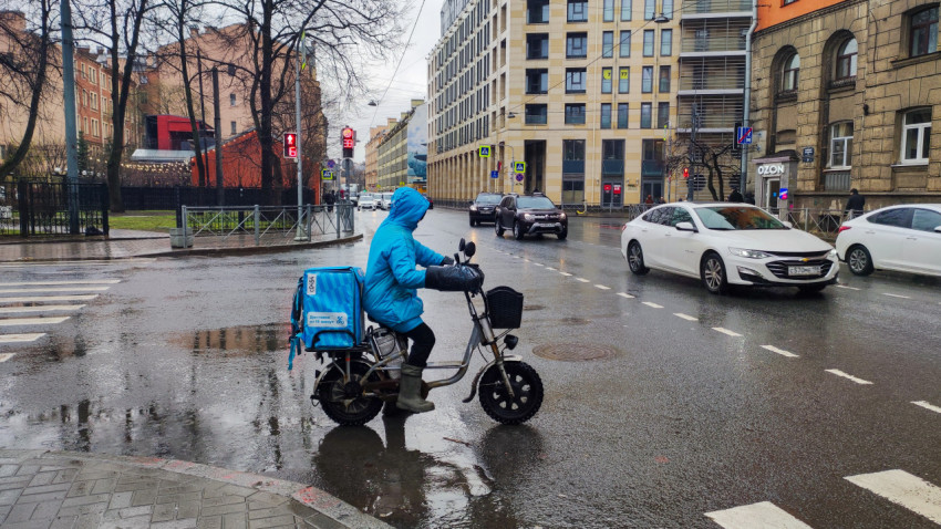 Курьер на электрическом велосипеде на перекрёстке в дождливый день