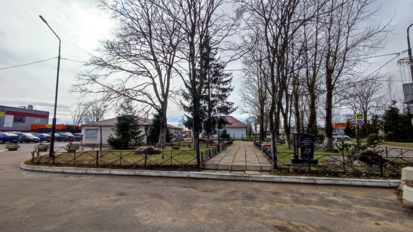 Мемориальный сквер с аллеей и деревьями в городской застройке