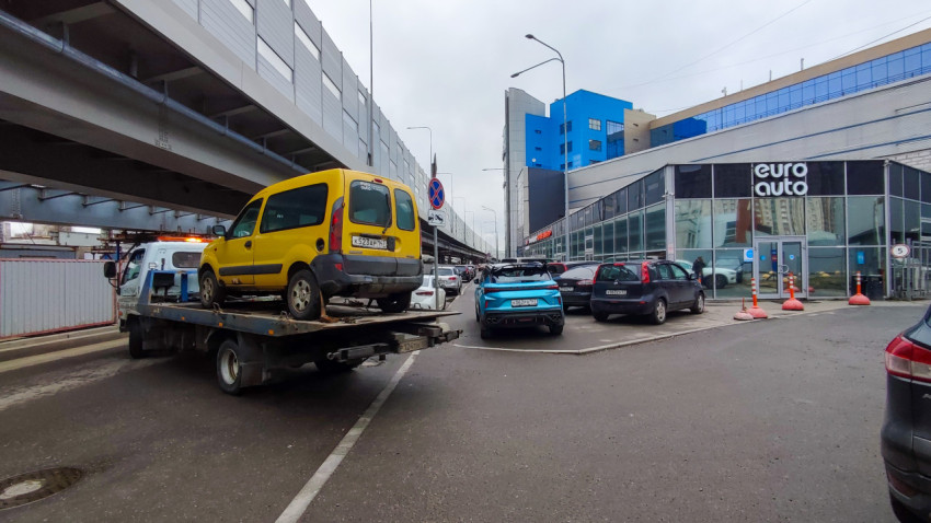 Эвакуатор с автомобилем у здания автосервиса и транспортной развязки