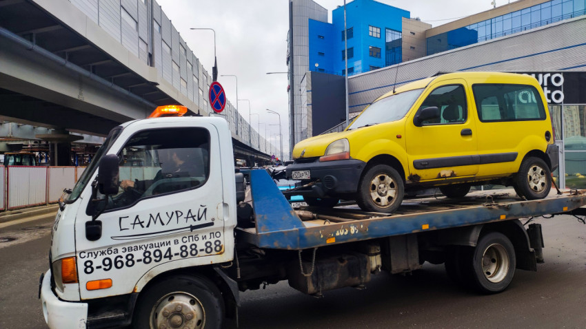 Эвакуатор перевозящий автомобиль возле городской эстакады и автосервиса