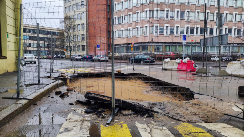 Провал дорожного покрытия у офисных зданий, ограждённый временным забором
