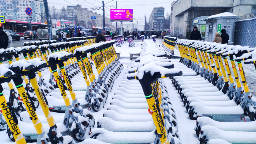 Зимняя парковка электросамокатов возле оживлённой городской улицы