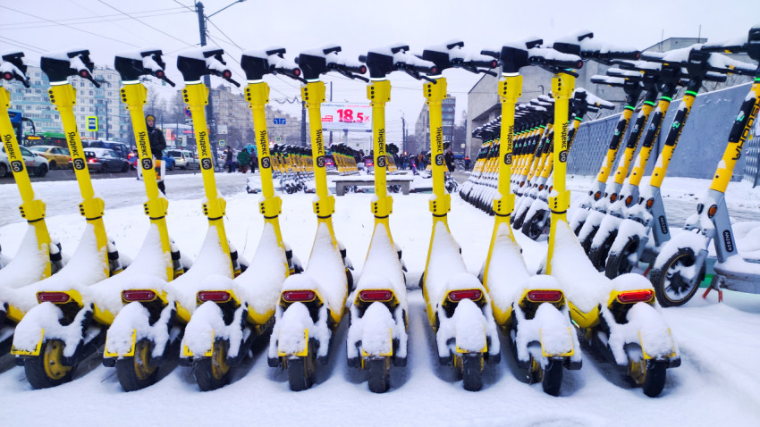 Жёлтые электросамокаты под снегом на фоне городского движения