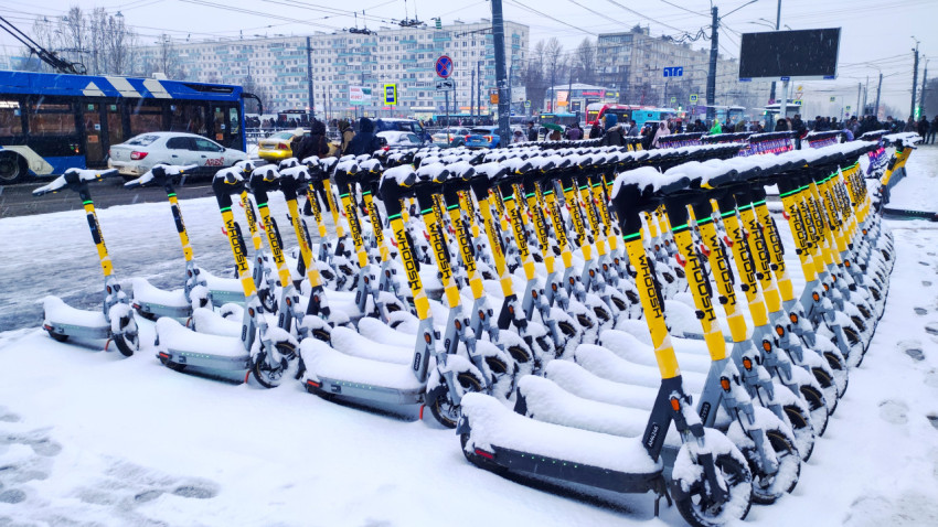 Стоянка электросамокатов под снегом у оживлённой магистрали