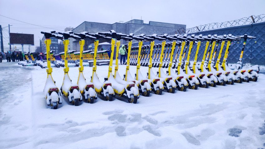 Зимняя стоянка электросамокатов на фоне промышленного здания