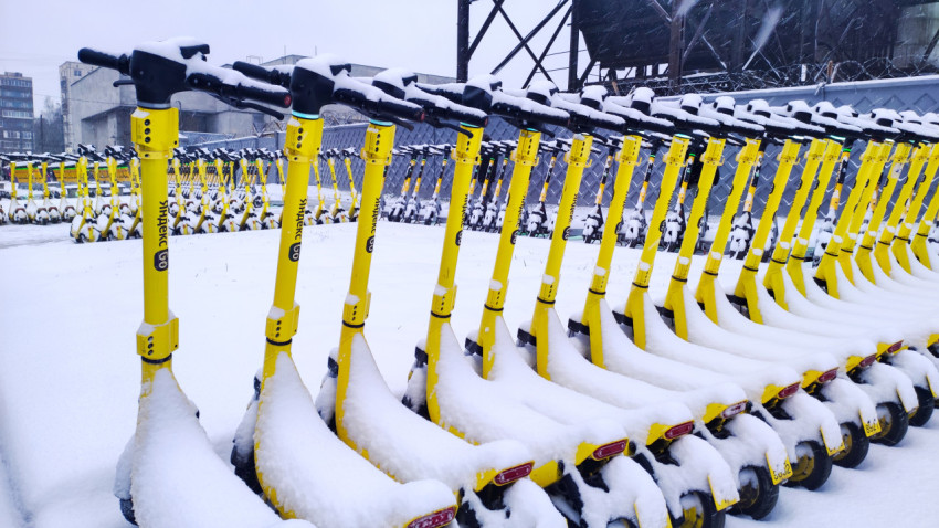 Электросамокаты под снегом на заснеженной площадке возле городских построек