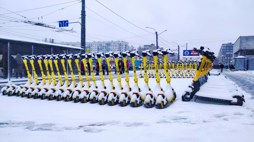 Электросамокаты Whoosh, покрытые снегом на зимней городской стоянке