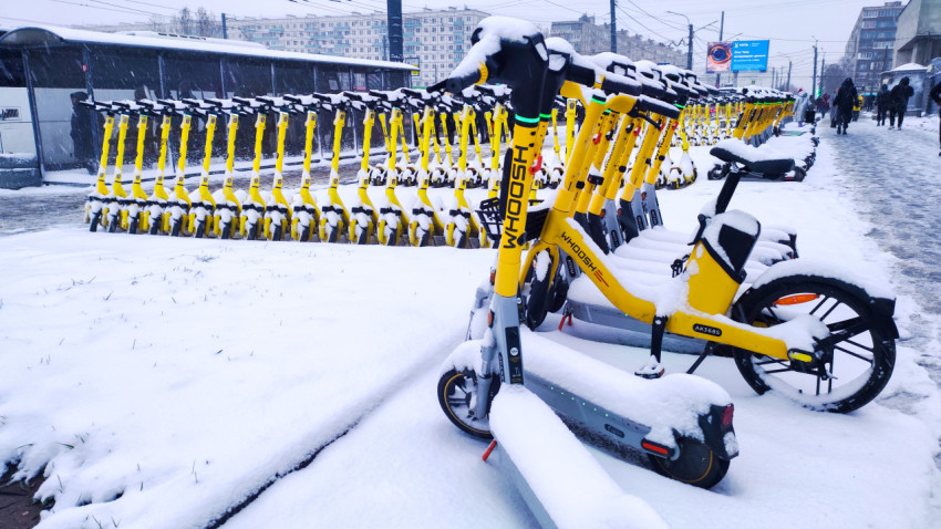 Электросамокаты Whoosh под снегом у остановки общественного транспорта