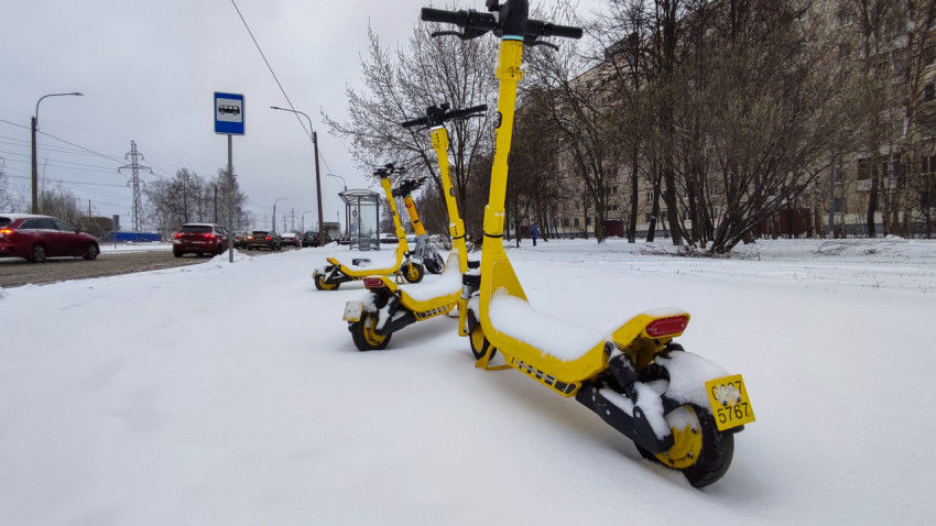 Электросамокаты «Яндекс Go» под снегом у дороги в жилом районе