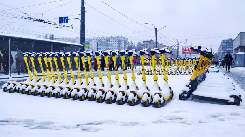 Заснеженный ряд арендуемых электросамокатов у остановки общественного транспорта