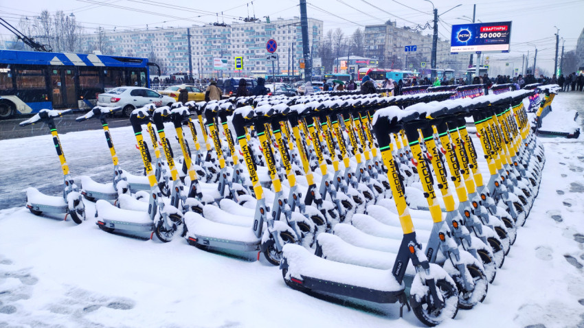 Ряды электросамокатов под снегом возле остановки троллейбуса
