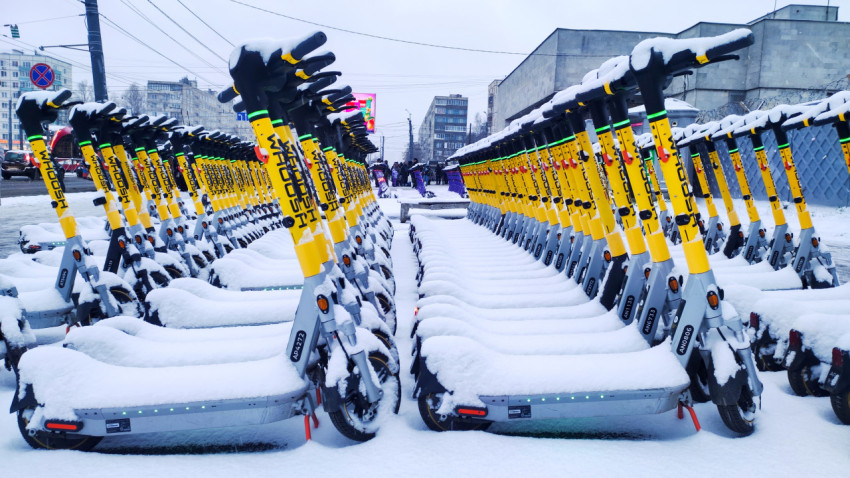 Парковка жёлтых электросамокатов под снегом в промышленном районе
