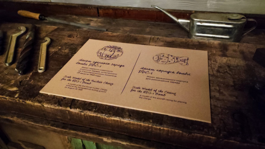 Табличка о макетах бомбы РДС-1 в окружении инструментов на рабочем столе