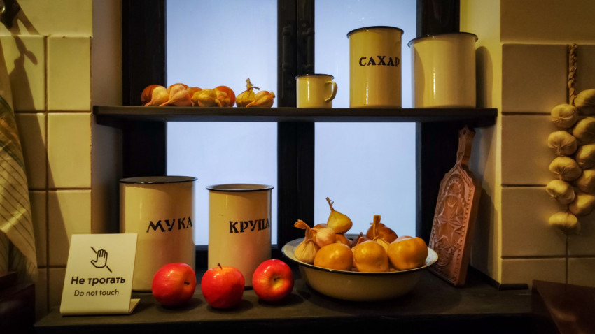 Полка с продуктами и металлическими банками в советской кухонной экспозиции