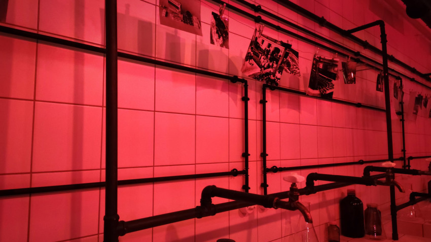 Стена фотолаборатории с трубами и развешенными фотографиями