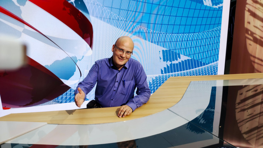 Мужчина у новостного стола на фоне графики глобуса в выставочной студии