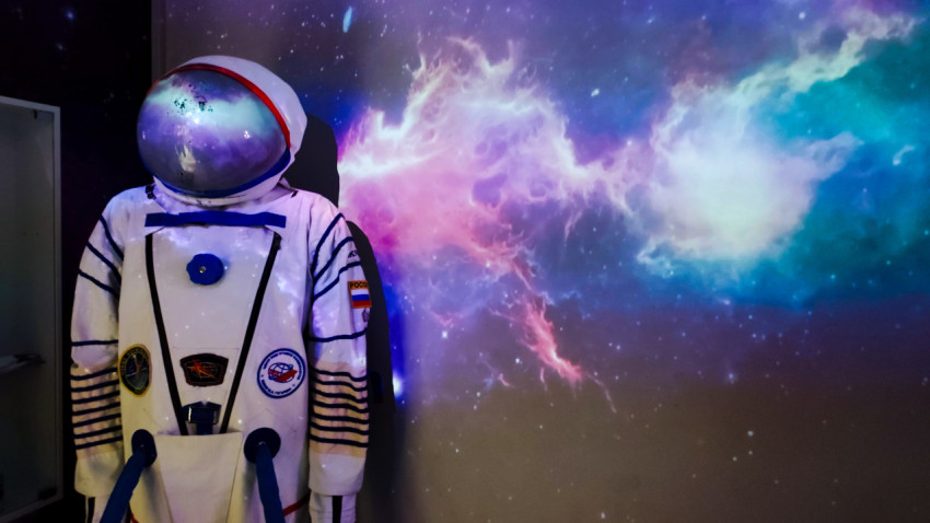 Манекен в космическом скафандре на фоне проекции звёздного неба