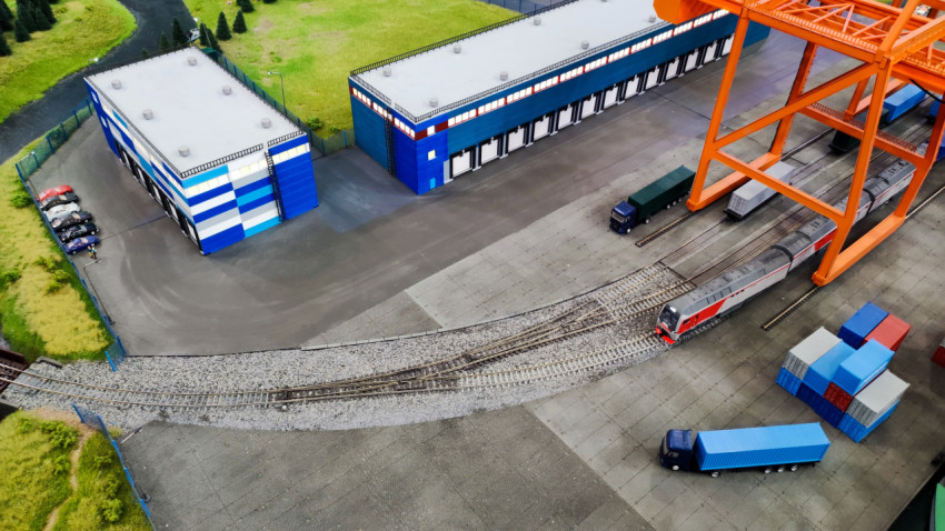 Железнодорожный локомотив и грузовые платформы под портальным краном в макете терминала