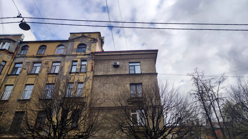 Фасады старых жилых домов с изношенной штукатуркой и деревьями на переднем плане