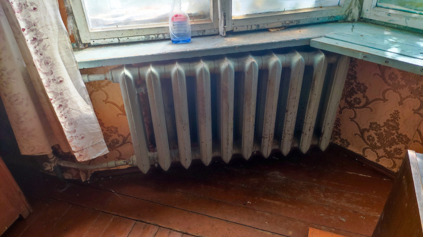 Радиатор под окном с занавеской и бытовыми предметами