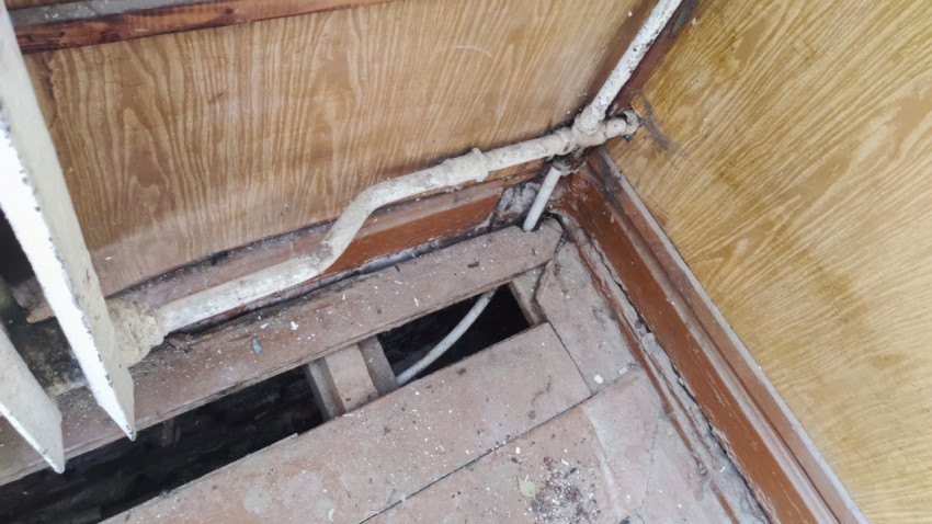 Поврежденный деревянный пол с открытым участком и трубами отопления