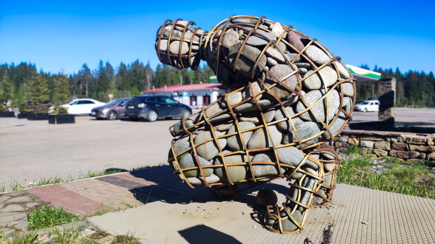 Скульптура из камней на фоне парковки и лесного массива
