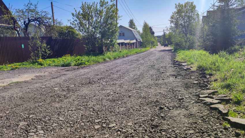 Загородная улица со щебёночным покрытием и жилой застройкой по обеим сторонам