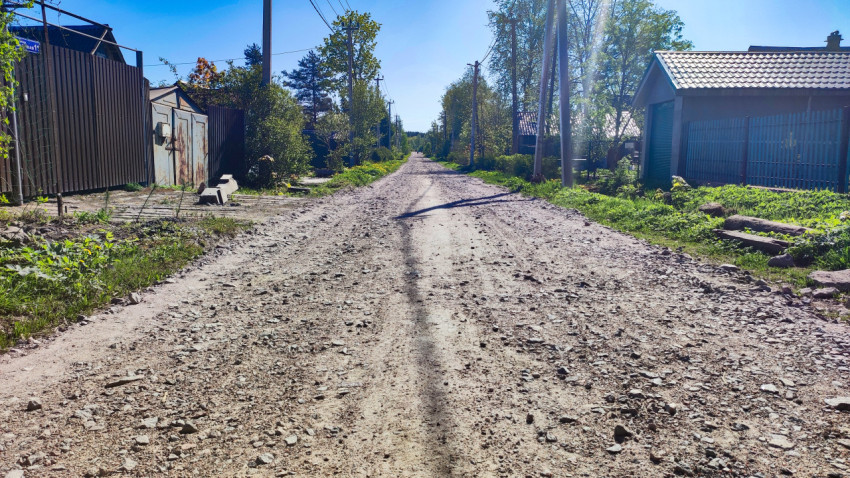 Длинная грунтовая улица с заборами, гаражами и многочисленными опорами ЛЭП