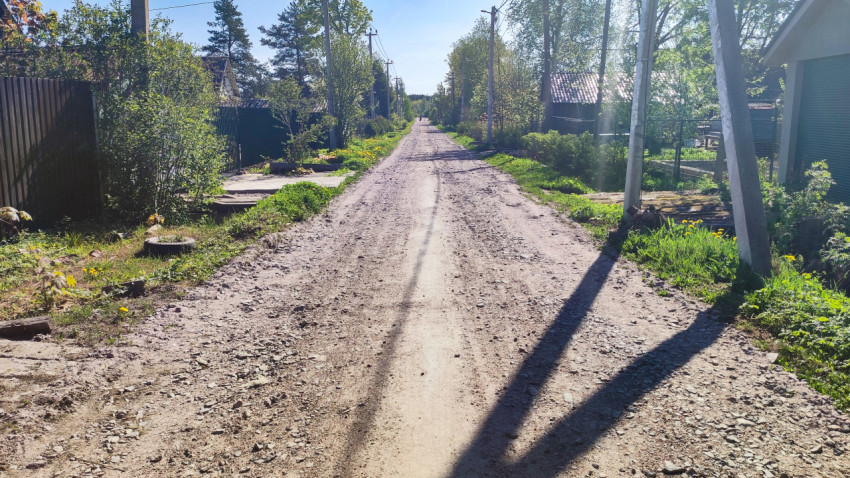 Грунтовая дорога частного сектора с опорами ЛЭП и зелёными обочинами