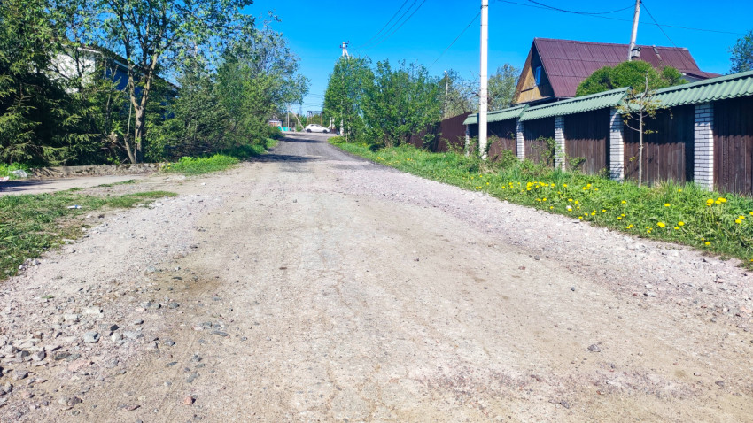 Просёлочная дорога с забором и жилыми строениями вдоль обочины