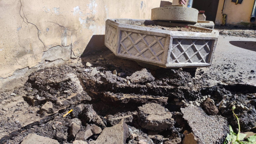 Бетонный вазон на участке демонтированного асфальта возле стены здания