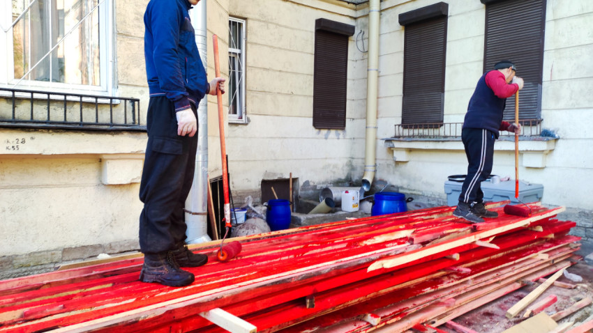 Рабочие окрашивают деревянные балки во дворе жилого дома