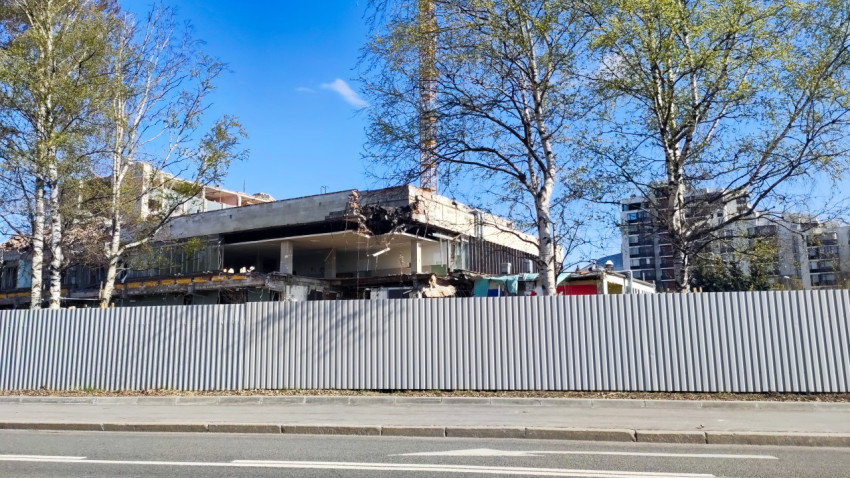 Демонтаж крупного здания за ограждением из профнастила