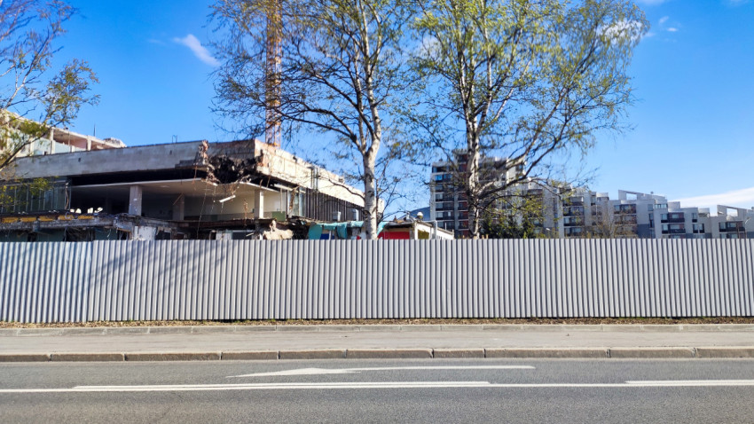 Строительная площадка с разборкой здания за металлическим ограждением