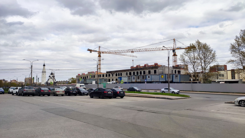 Стройплощадка с башенными кранами и парковкой на фоне городской застройки
