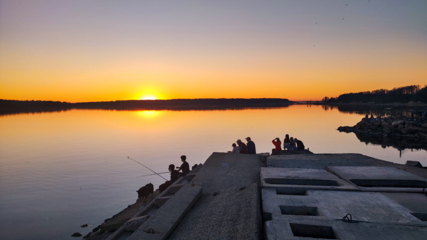 Люди на берегу водоёма во время заката