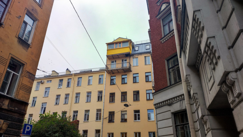 Двор-колодец с фасадами старых домов, проводами и жёлтой застеклённой надстройкой балкона