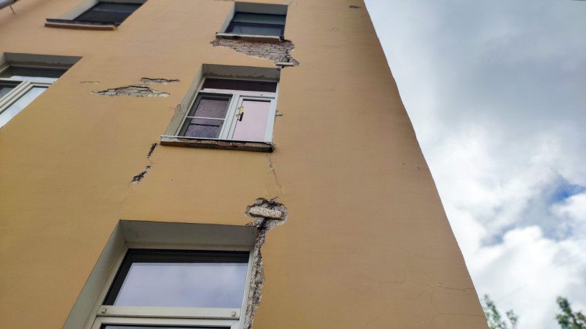 Крупный план трещин и осыпающейся штукатурки на фасаде вокруг окна многоэтажного дома
