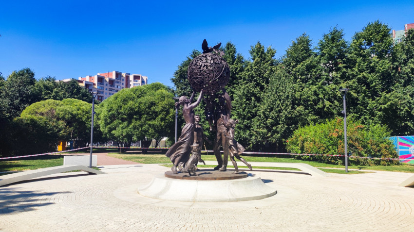 Скульптура «Семья — залог мира» на круговой площадке Парка 300-летия Санкт-Петербурга на фоне деревьев и жилых домов