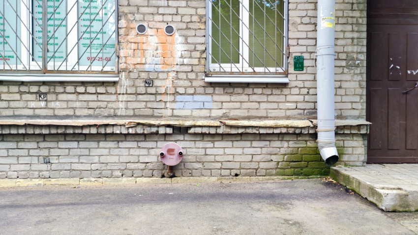 Кирпичный фасад здания с окнами в решётках и водосточной трубой
