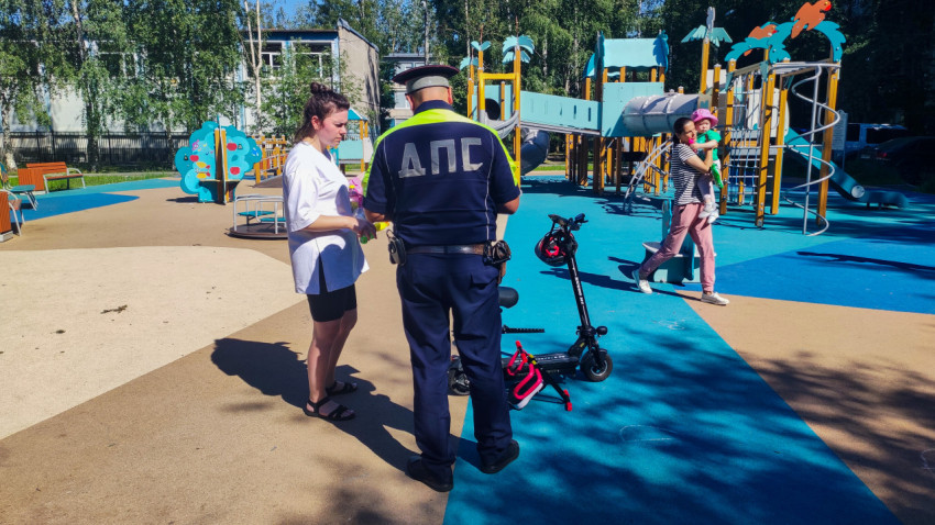 Сотрудник ДПС и женщина стоят на детской площадке возле электросамоката и шлема