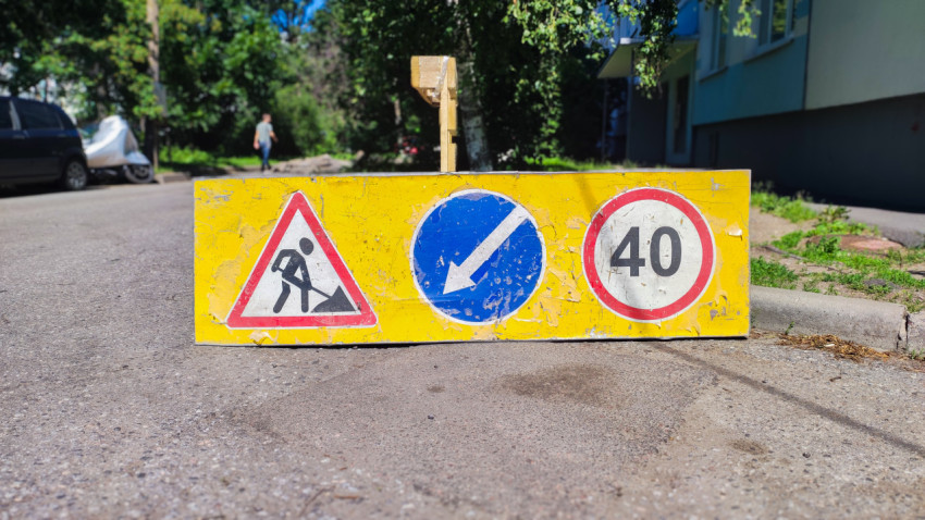 Потёртый жёлтый щит дорожных работ со знаками объезда и ограничения скорости 40 во дворе
