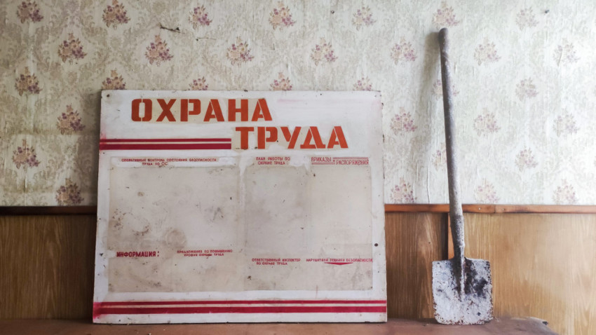 Стенд «Охрана труда» и старая лопата у стены в заброшенном помещении