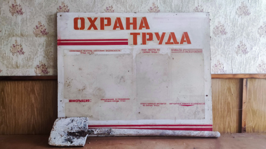 Стенд «Охрана труда» и лопата на столе на фоне выцветших обоев