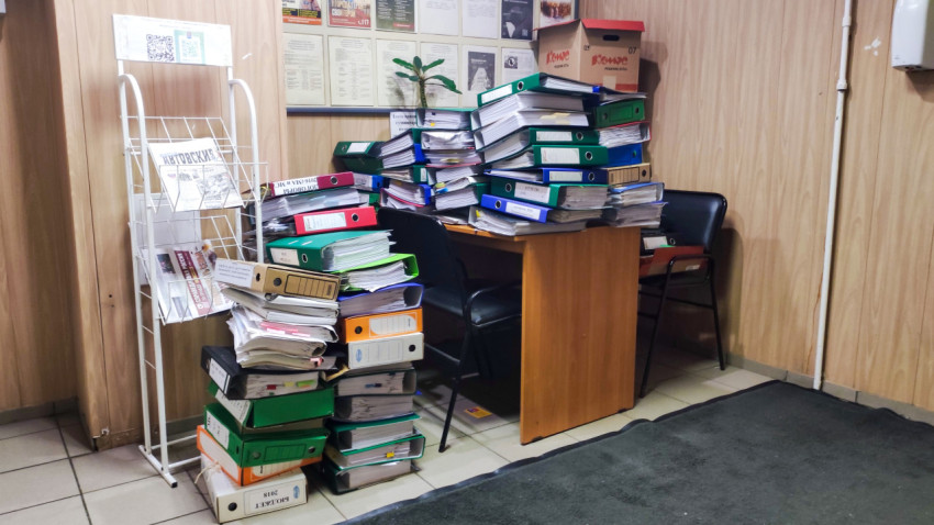 Пачки папок и документов в офисе на столе и стульях рядом с информационным стендом
