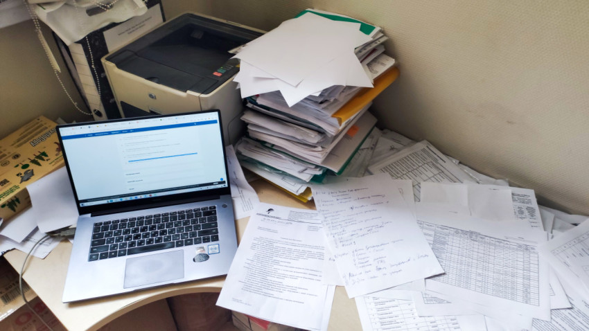 Рабочий стол с ноутбуком, принтером и стопками бумажных документов в офисе