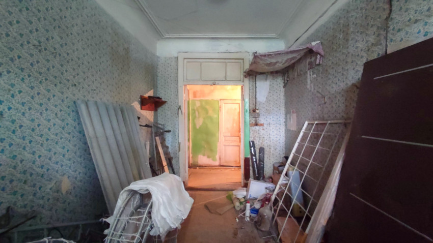 Комната с обоями и строительным хламом, снятая на фоне коридора с обшарпанными дверями