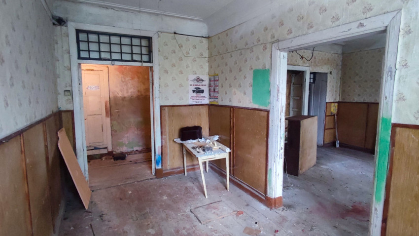 Пустое помещение с несколькими дверными проёмами, столом и плакатами на стенах