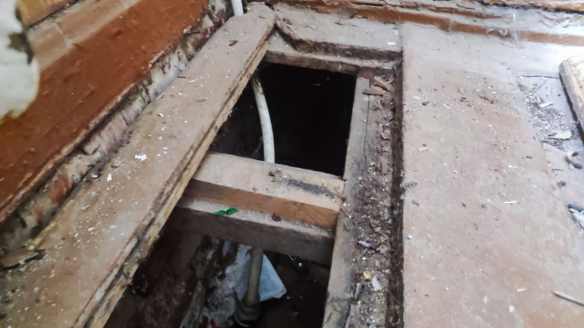 Отверстие в деревянном полу с видимыми балками и трубами коммуникаций